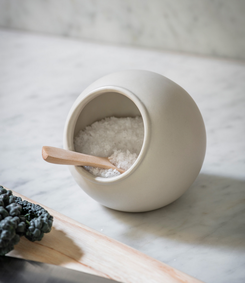 White ceramic container with a wooden spoon on a marble surface