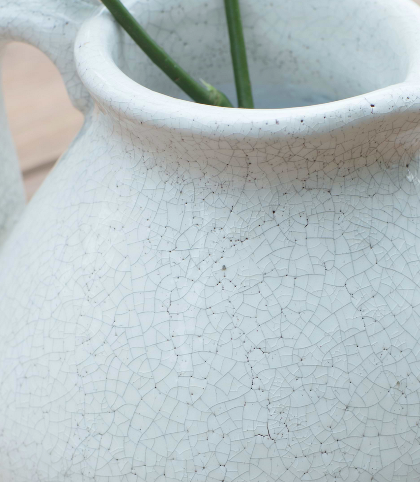 Close-up of a textured white ceramic vase with a plant stem inside.
