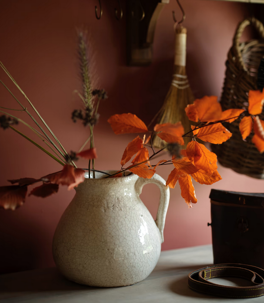 White ceramic pitcher with orange leaves against a pink wall