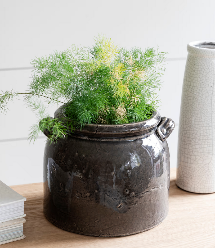 Decorative pot with greenery on a wooden surface next to a textured vase.