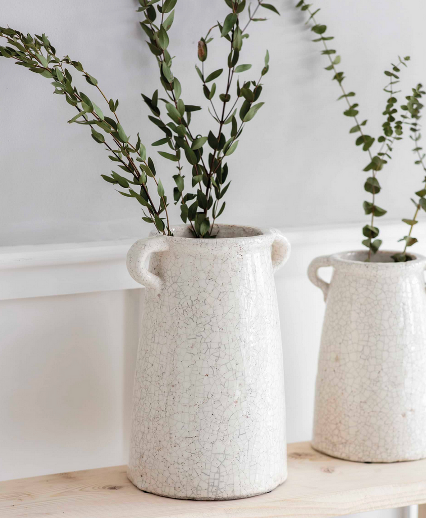 Two textured white planters with greenery on a light wooden surface.