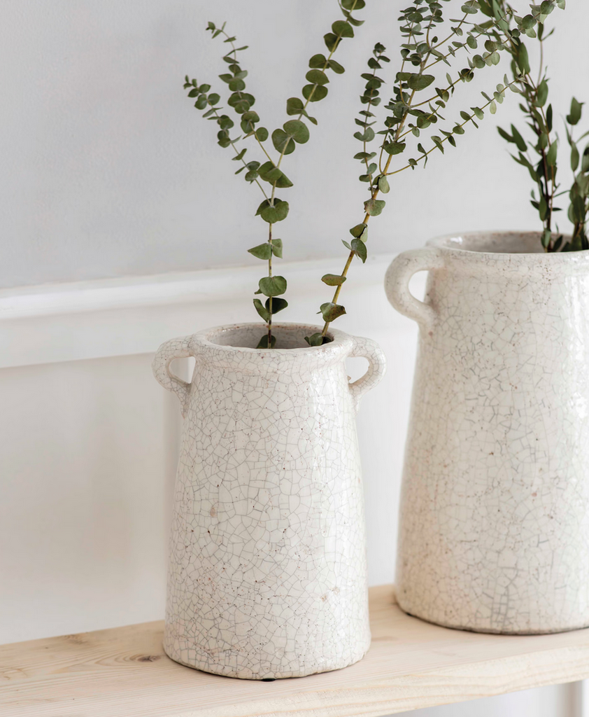 Two textured ceramic vases with plants on a wooden surface.