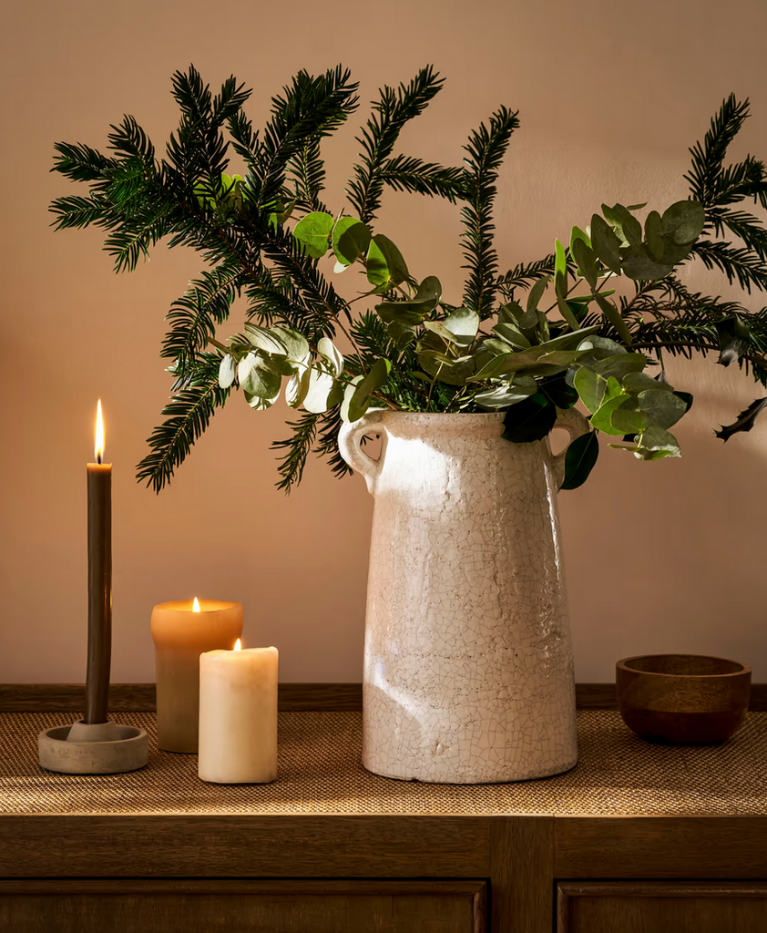 White vase with greenery on a wooden surface with candles