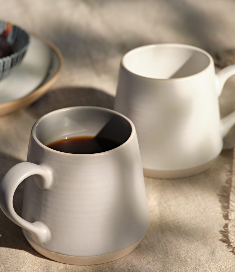 Two ceramic mugs on a textured surface, one filled with coffee.