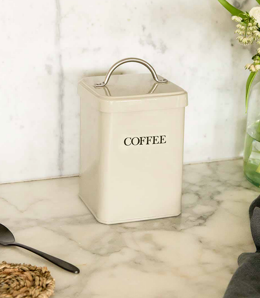 Beige coffee canister on a marble surface with a vase of flowers in the background